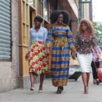 "Trois femmes africaines marchant en ville, arborant un mélange de mode contemporaine et d'imprimés traditionnels colorés pour un article sur l'art de vivre."