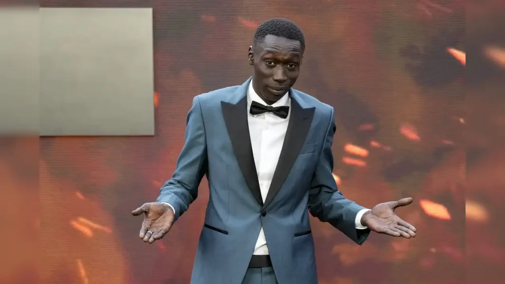 évaluation de l'économie des influenceurs: La sensation mondiale des réseaux sociaux Khaby Lame, souriant et faisant un signe de paix en sweat à capuche gris ; illustrant l'essor de l'économie des créateurs africains et l'influence numérique mondiale.