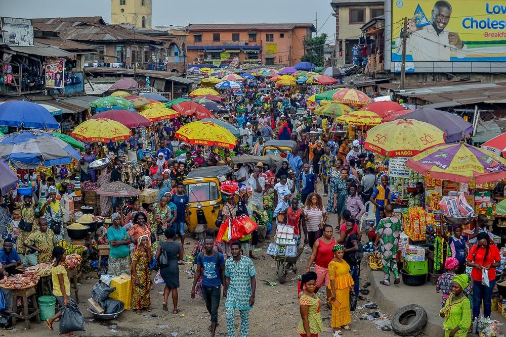 Numérisation : L’unique et explosif virage à 97 millions de dollars des États nigérians numérisation: Une vue en plongée du marché bondé de Mushin à Lagos, au Nigeria, rempli de parasols colorés, de vendeurs et d'acheteurs ; illustrant l'ampleur du commerce de proximité en Afrique de l'Ouest