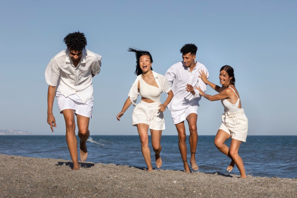 Durabilité: Un groupe diversifié de jeunes adultes joyeux en tenue d'été blanche élégante courant le long d'une plage ensoleillée ; représentant le tourisme côtier dynamique et le style de vie premium en Afrique.