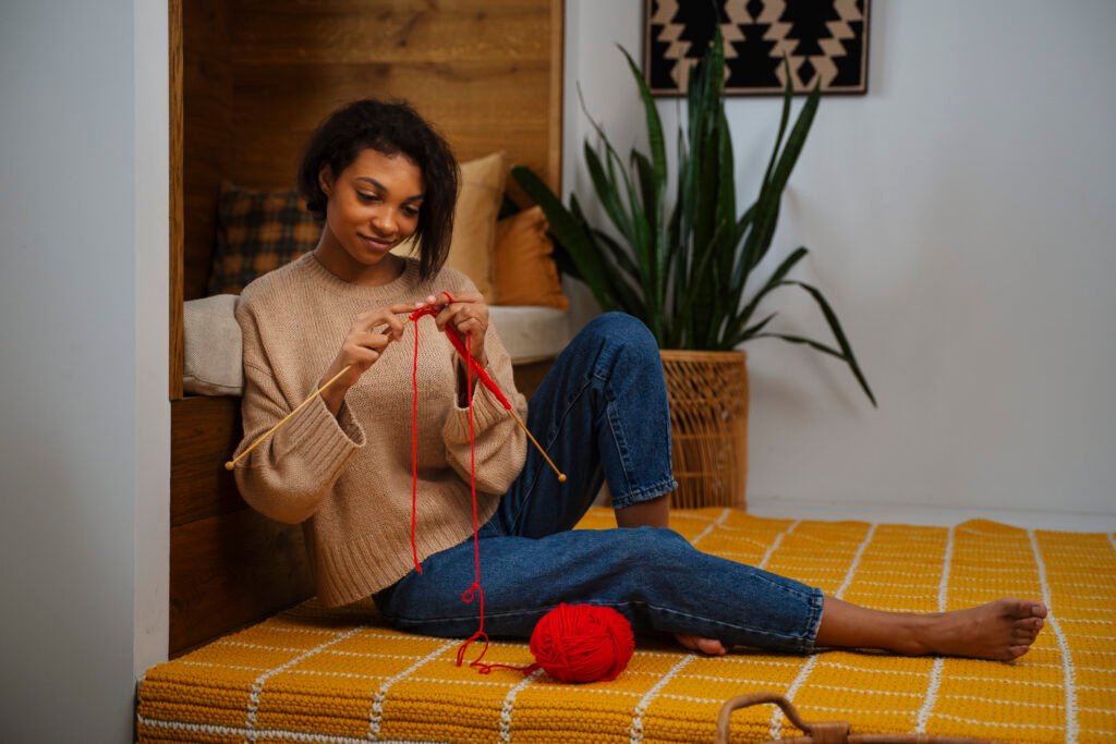 Tricot: Jeune femme tricotant avec de la laine rouge dans une maison moderne. »