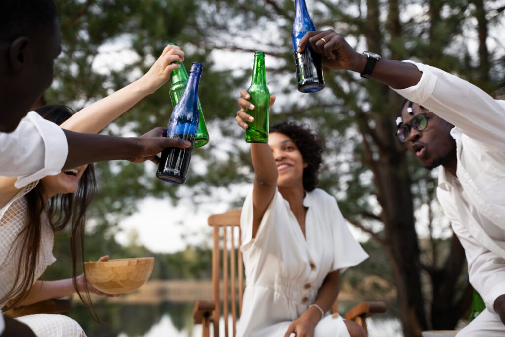 Alcool: Vue en contre-plongée d'amis portant un toast avec des bouteilles de bière et de soda lors d'une réception, illustrant la croissance des secteurs des boissons premium et du divertissement social en Afrique.