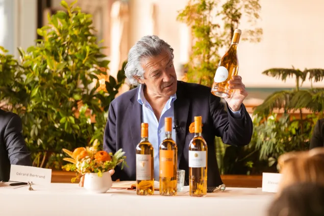 VIN : La révolution du sans alcool menée par Bertrand Degat au 21st century. win: Un gros plan de Gérard Bertrand discutant de la qualité viticole avec plusieurs bouteilles de vin sur une table ; représentant le leadership dans l'agriculture durable et les standards de produits premium.